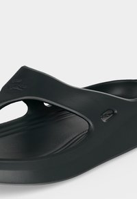 Μαύρο σανδάλι slip-on με περιμετρικό πέλμα, ανοιχτές πλευρές και ανάγλυφο λογότυπο στο λουράκι, σχεδιασμένο για καθημερινή χρήση.