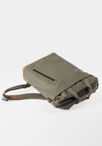 Olivgrüner Rucksack mit Leder-Akzenten, oberen Griffen, gepolstertem Schulterriemen und einer vorderen Reißverschlusstasche, flach liegend auf weißem Hintergrund.