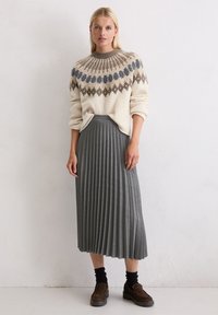 Gebreide trui in crème met grijze en bruine geometrische patronen; geplooide grijze rok tot halverwege de kuit; bruine schoenen en zwarte sokken.