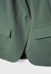 Blazer vert à fermeture à un bouton et deux poches à rabat sur le devant, visible de la taille à l'ourlet.