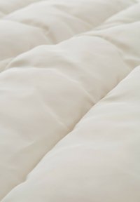 Couette blanche matelassée avec une texture lisse et douce. Le tissu présente des motifs de couture subtils, améliorant son design global et sa couverture.