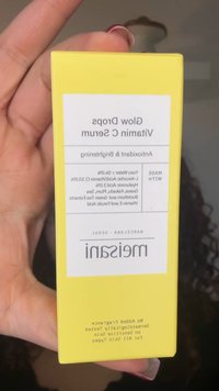 Gult rektangulært merke merket "Glow Drops Vitamin C Serum." Tekst som inkluderer ingredienser og bruksdetaljer, trykt i svart på hvit bakgrunn.