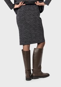 Stivali alti fino al ginocchio in pelle marrone con una finitura liscia, punta quadrata e suola bassa e spessa nera. Indossati con una gonna a maglia grigio scuro testurizzata.