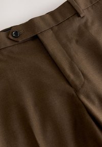 Pantalon marron sur mesure avec ceinture, fermeture par bouton et braguette zippée à l'avant, présenté en gros plan.