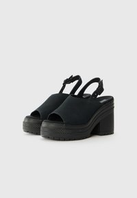 Sandales à plateforme noires avec un orteil ouvert, tige en tissu, une sangle arrière réglable et une semelle en caoutchouc texturée.