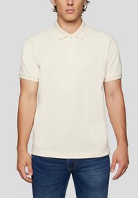 Cremefarvet bomulds-polo med klassisk krave, korte ærmer og en lille logo-detalje på brystet. Krydret med blå denim jeans.