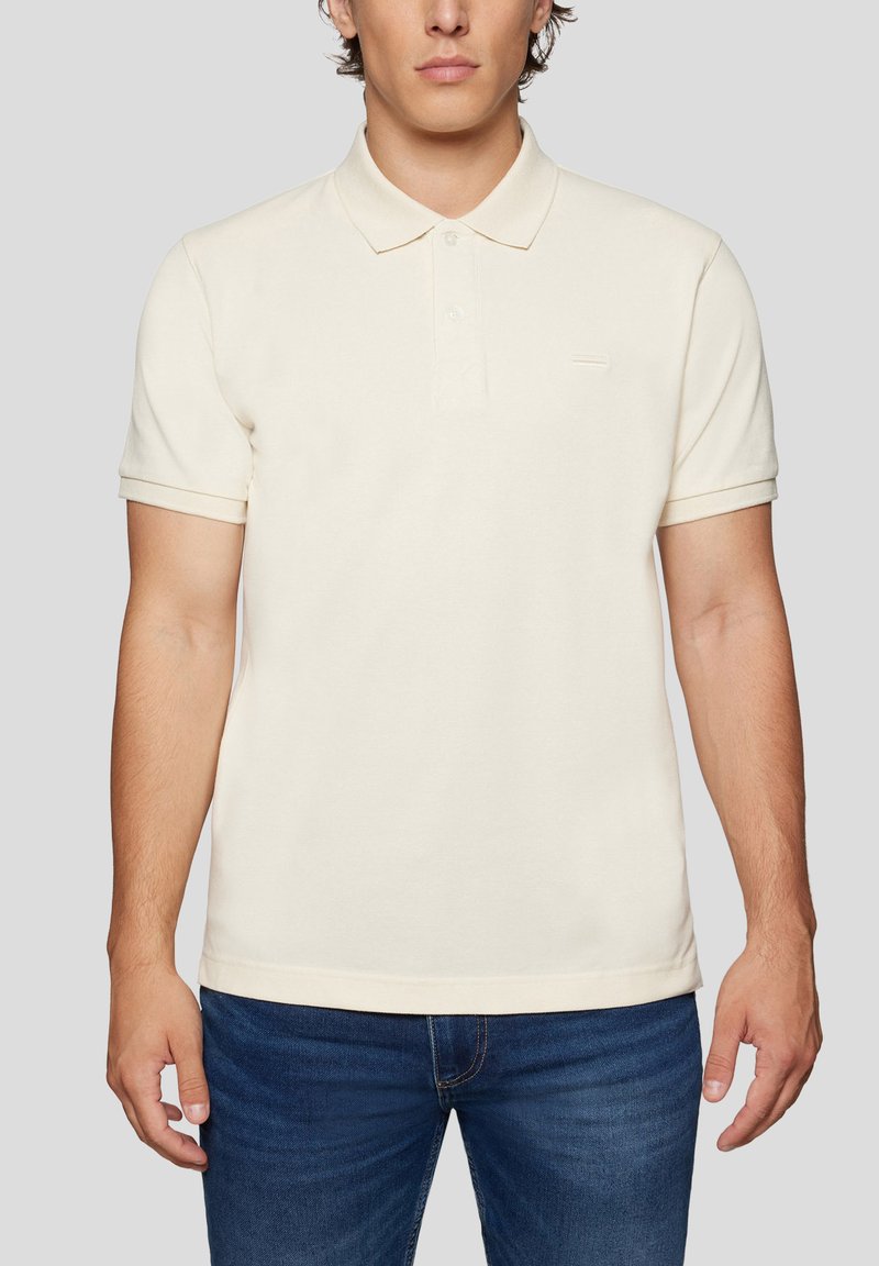 Cremefarvet bomulds-polo med klassisk krave, korte ærmer og en lille logo-detalje på brystet. Krydret med blå denim jeans.