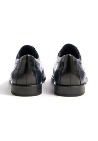 Zwarte en marineblauwe leren schoenen met een gladde textuur, afgeronde hakken en stikseldetails. Achteraanzicht toont het ontwerp met twee kleuren.