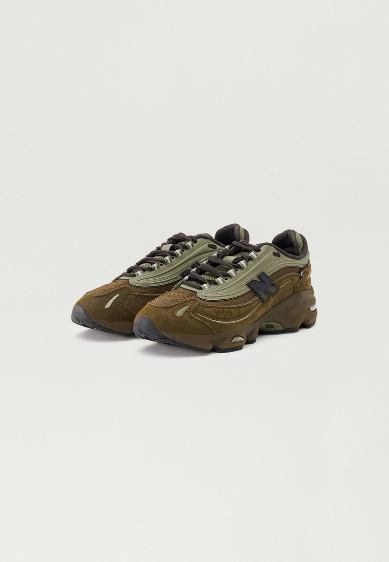 Sneakers verdi e marroni con tomaia in suede e mesh, lacci tondi e suola in gomma nera con scanalature per la trazione.