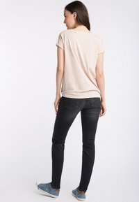 Jasnoróżowa koszulka z krótkim rękawem, noszona z ciemnymi, dopasowanymi dżinsami i niebieskimi trampkami. Prosty, miękki materiał o luźnym kroju.