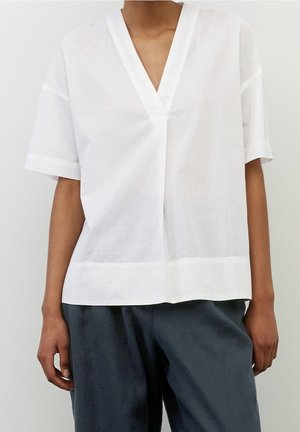 Blusa blanca de manga corta hecha de tejido ligero, con un escote en V profundo, corte recto y detalles sutiles en el dobladillo.