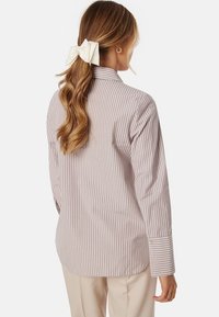 Camicia a maniche lunghe a righe in beige chiaro e bianco, con una vestibilità leggermente ampia, polsini con bottoni e design del colletto classico.