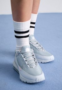 Light gray Nike sneakers with mesh upper, pink accents, and textured sole, paired with white socks featuring black stripes.