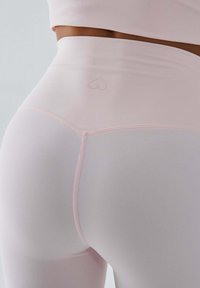 Jasnoróżowe legginsy z wysokim stanem wykonane z elastycznego materiału o gładkiej fakturze. Na pasku znajduje się delikatne logo w kształcie serca wyszyte haftem.