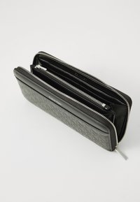 Black leather wallet with quilted pattern, zipper closure, and dual compartments. Features silver-tone hardware and embossed logo detail.