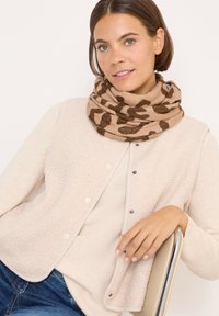 Beige fleecevest med trykknapper over en lys sweater, parret med et tørklæde i brun leopardmønster. Bløde teksturer og hyggeligt design.