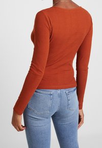 Top a manica lunga in ruggine a coste con design aderente, caratterizzato da un collo rotondo e una texture liscia, abbinato a jeans aderenti di un blu chiaro.