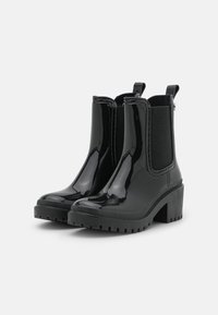 Black rain boots with a glossy finish, featuring elastic side panels, a chunky heel, and textured rubber soles for traction.
