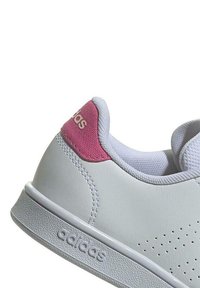 Zapatilla blanca con acento rosa en el talón, con parte superior sintética suave, diseño perforado, cuello acolchado y suela de goma con el logotipo de la marca.