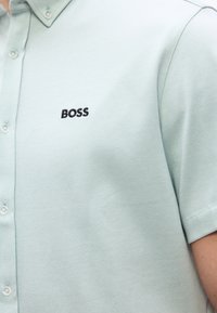 Ελαφρύ πουκάμισο κοντομάνικο σε μέντα πράσινο χρώμα με κουμπιά και κεντημένο μαύρο κείμενο "BOSS" στο αριστερό στήθος.