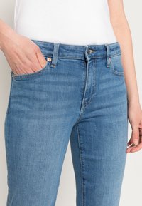 Jeans de ganga azul claro com um design ajustado, apresentando um estilo de cinco bolsos, costura visível e fecho de botão e fecho éclair.