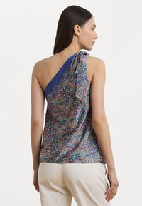 One-shoulder top in vibrant paisley pattern, featuring a blue shoulder band and soft fabric. Back view shows draping details and fitted shape.