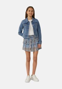 Denimjack met twee voorkruiszakken, gelaagde roestrokken in een multikleurig patroon en witte sneakers, wat een casual outfit creëert.