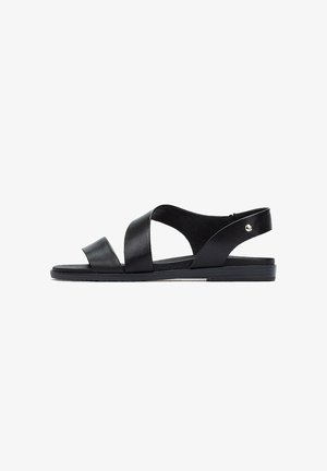 Las sandalias de cuero negro presentan correas entrelazadas y una correa trasera, con una suela plana y un minimalista acento de hardware en el lateral.