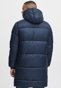 Giubbotto imbottito blu navy con cappuccio, caratterizzato da un design trapuntato e cuciture orizzontali. Texture liscia, lunghezza fino al ginocchio con polsini a costine.