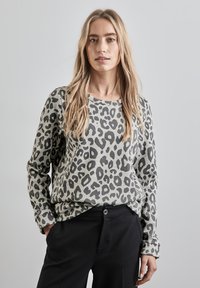 Maglione pullover con stampa leopardata grigia chiara e macchie nere, con scollatura rotonda e maniche lunghe, abbinato a pantaloni neri.