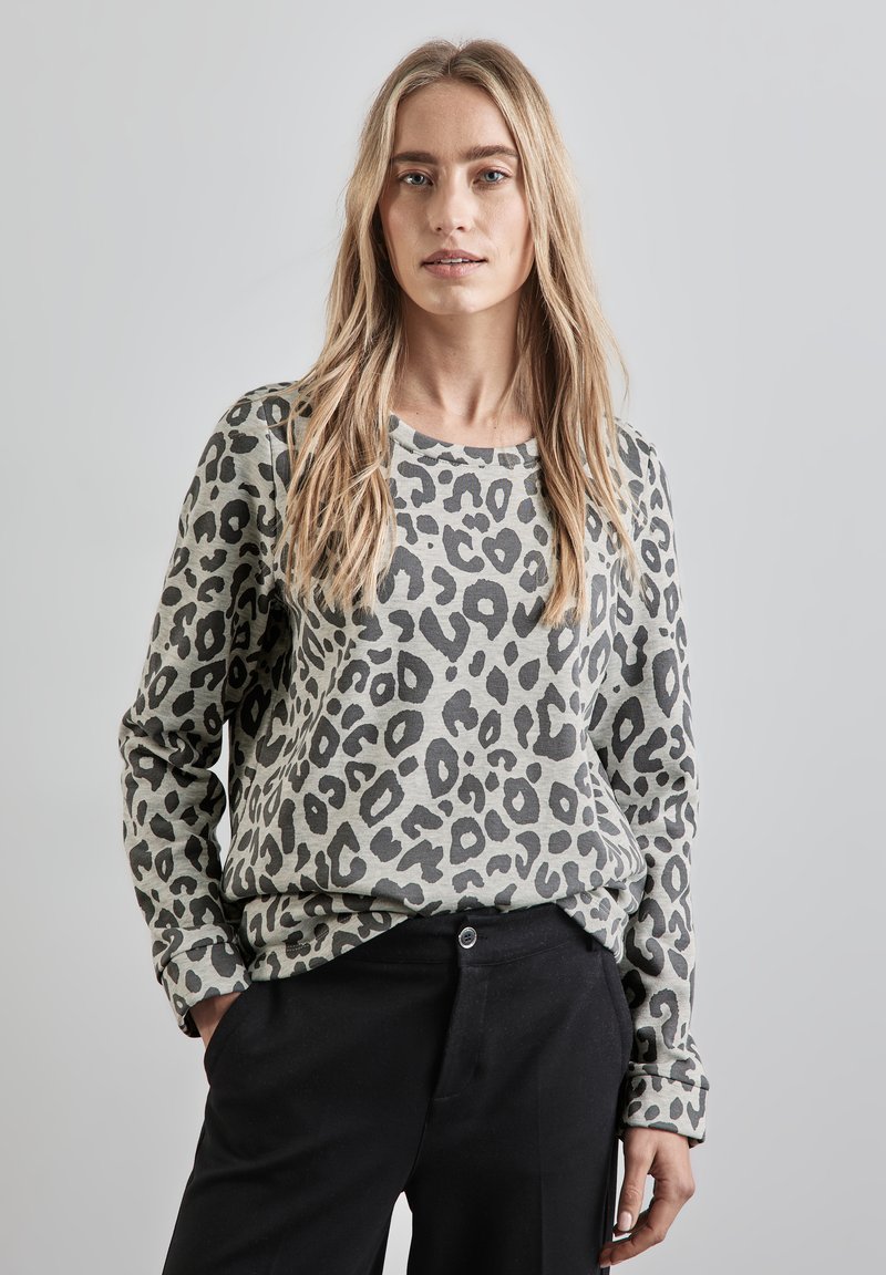 Suéter de punto con estampado de leopardo en gris claro con manchas negras, con cuello redondo y mangas largas, combinado con pantalones negros.