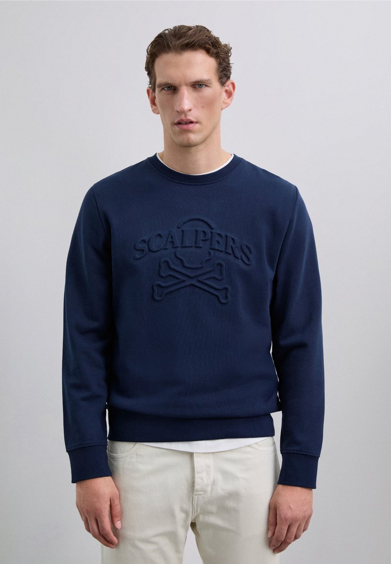 Sweatshirt bleu marine avec un logo texturé représentant un crâne et des os croisés. Col ras du cou, poignets côtelés et tissu doux et lisse.