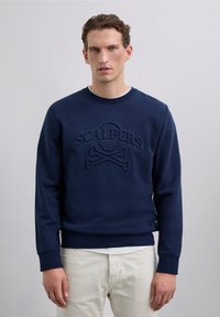Sudadera de color navy con un logo texturizado que presenta una calavera y tibias cruzadas. Cuello redondo, puños de canalé y tejido suave y liso.