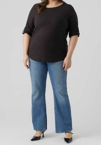 Maglietta nera a tre quarti con maniche arrotolate, abbinata a jeans a zampa di elefante azzurri e décolleté nere a punta. Outfit semplice e casual.