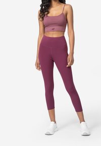 Top corto de canalé de cuello alto y leggings de tiro alto en tela burdeos. Presenta una textura suave, silueta ajustada y un minimalismo en la marca.