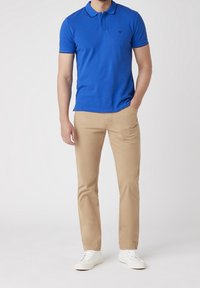 Blå pikétröja med korta ärmar, med krage och ett litet emblemet på bröstet, i kombination med khakifärgade byxor och vita sneakers.