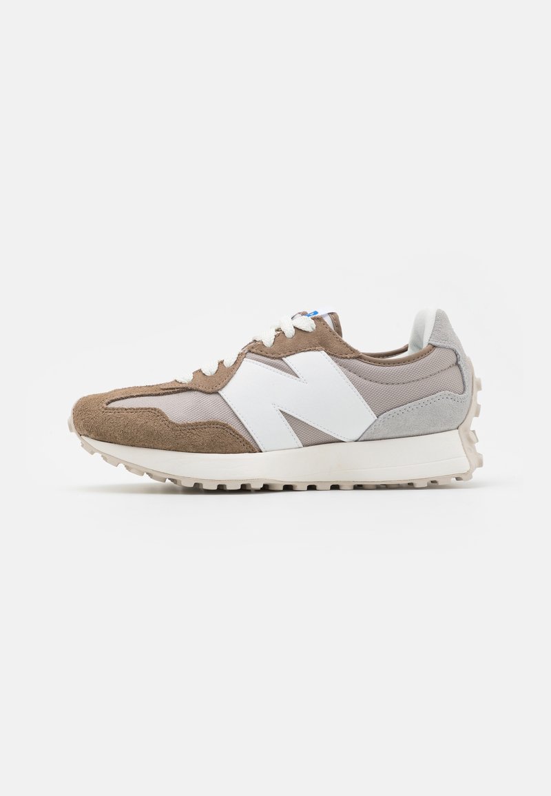 Vue latérale d'une basket sportive beige et grise avec des lacets blancs et un grand "N" blanc sur le côté, reposant sur une surface blanche.