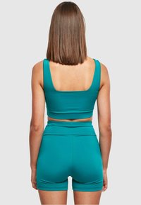 Tyrkysový crop top a zodpovedajúce krátke nohavice s vysokým pásom, vyrobené z hladkej tkaniny s priliehavým strihom. Minimalistický štýl s širokými ramienkami a štvorcovým chrbtom.