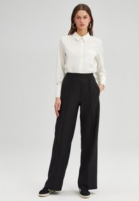 White long-sleeve button-up shirt with a collar and a chest pocket, paired with black elastic-waist wide-leg trousers and black sneakers.