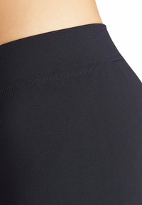Leggings de sport noirs dotés d'un tissu lisse et extensible avec une large ceinture sans coutures. La texture est mate avec un léger éclat.
