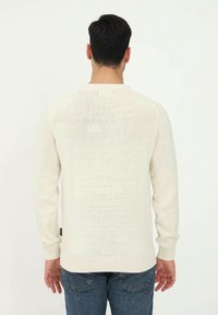 Helle beige Strickjacke mit strukturiertem Maschenbild, Rundhalsausschnitt, langen Ärmeln und enganliegenden Bündchen, kombiniert mit blauen Jeans.