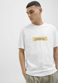 Hvid bomulds t-shirt med et rektangulært gult logo med sort tekst "Jack&Jones" på brystet, korte ærmer og en afslappet pasform.