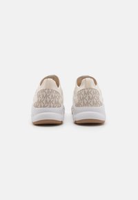 Krémové slip-on tenisky s texturovaným elastickým svrškem, na kterém se opakuje logo MK, bílé mezipodešví a světle hnědou gumovou podrážkou.