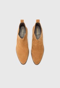 Bottines en daim marron avec un bout pointu, des panneaux latéraux élastiques et une semelle en caoutchouc plate. L'étiquette à l'intérieur indique "ANNA FIELD."