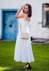 Bílá bezrukávová šaty s lehkým sukní, v kombinaci se světle béžovou kabelkou přes rameno a černými sandály na podpatku, položené na zelené trávě.