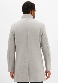 Cappotto in misto lana grigio chiaro con alto colletto, maniche lunghe e taglio dritto. Presenta linee pulite e dettagli di cucitura sottili.