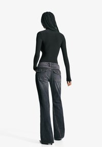 Svart långärmad topp i kombination med mörkblå utsvängda jeans, med bakfickor och subtila sömmar. Slät textur och figurnära design.