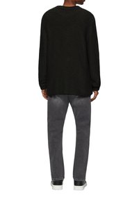 Schwarzer, gestrickter Pullover mit rundem Hals und langen Ärmeln, kombiniert mit grauen Jeans. Die Sneakers haben ein schwarz-weißes Farbschema.