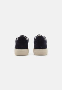 Adidași din suede bleumarin cu talpă din cauciuc bej și exterior texturat, având un design low top și căptușeală albă în contrast.