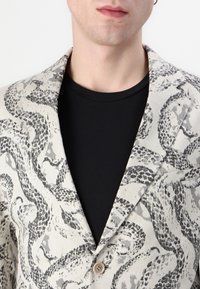 Blazer s hadom vzoru hada v čiernej farbe na svetlobeige pozadí. Má jedno gombíkové zapínanie a klasický golier.